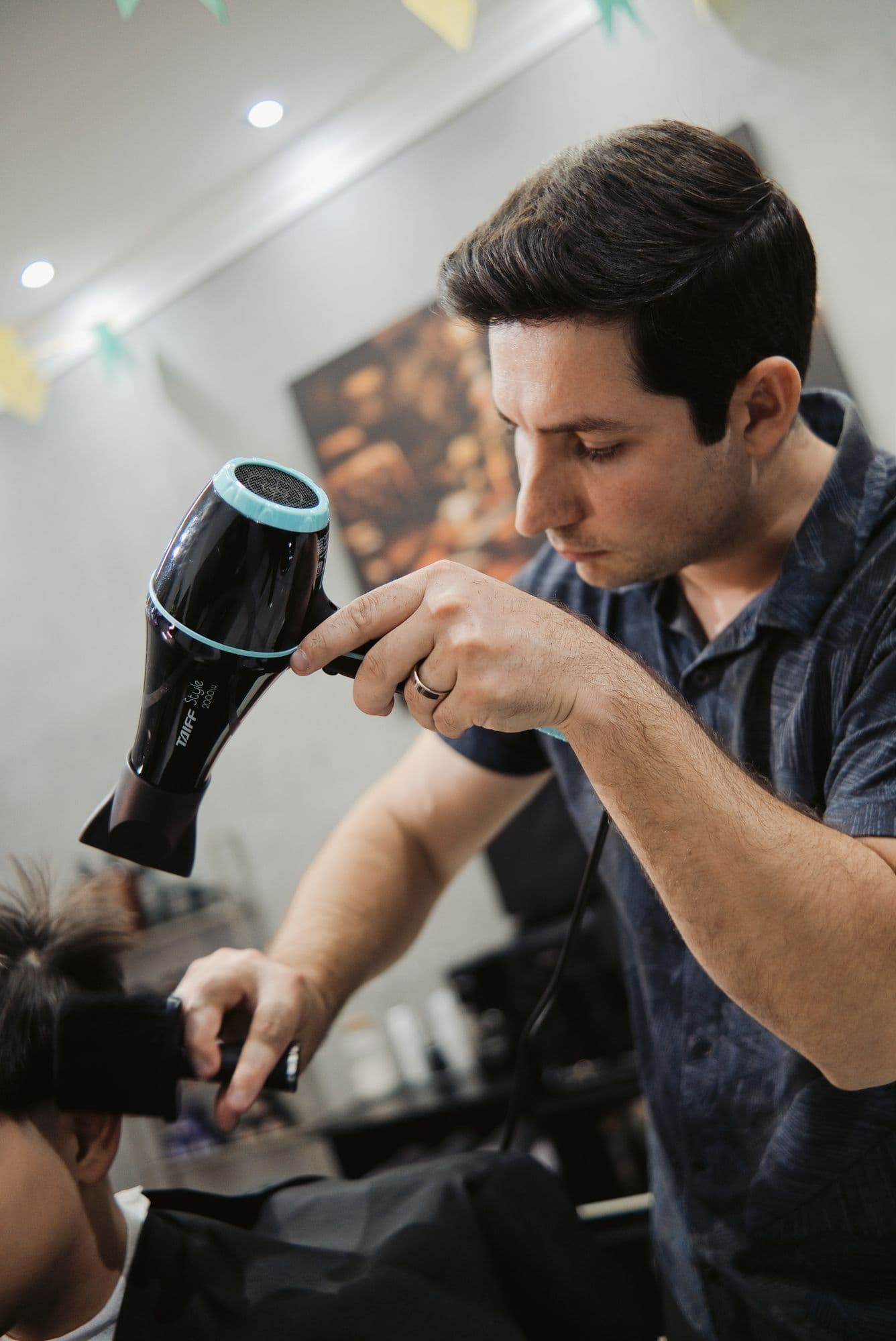 Barbeiro finalizando o penteado de um cliente com secador